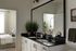 Modern bathroom with sleek black countertop, dual sinks, and stylish decor including vibrant plant accents and a large mirror, leading to a cozy bedroom with natural light.