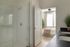 Modern apartment bathroom with glass shower and chic double vanity, leading to a cozy bedroom with lush greenery and ample natural light.