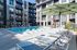 Modern apartment complex with luxurious poolside seating, surrounded by sleek, multi-story buildings and lush greenery.