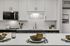 Modern kitchen with sleek white cabinetry and elegant tile backsplash, featuring a well-equipped countertop set for dining.