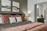 Elegant bedroom with plush bedding, abstract art, and a cozy atmosphere leading to a modern en-suite bathroom.
