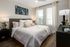 Chic modern bedroom with elegant decor featuring a plush bed, vibrant abstract art, and abundant natural light from large windows.