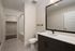Modern bathroom featuring sleek black cabinetry, elegant white countertops, a large mirror, and a spacious walk-in closet.