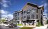 Modern apartment complex with sleek architecture, large windows, and a welcoming entrance under a blue sky.