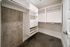 Modern walk-in closet with sleek white shelves, drawers, and ample hanging space against an industrial concrete wall.