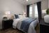 Elegant bedroom with stylish decor, featuring a plush bed with textured pillows, ambient lighting, and large windows with panoramic city views.
