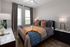 Elegant bedroom with a cozy ambiance featuring a plush bed with pillows and throws, modern nightstands, and chic d&eacute;cor elements. Natural light fills the space through large windows, highlighting the stylish wooden flooring.