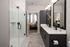 Elegant modern bathroom with sleek double vanity, spacious glass shower, and view into a cozy bedroom.
