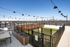 Charming rooftop patio with string lights, cozy seating, and stunning city views on a bright day.