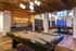 Chic recreation area featuring a modern billiards table, cozy dining setup, and ambient lighting under a stylish brick ceiling.
