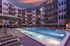 Luxurious apartment complex showcasing a serene swimming pool area with stylish lounge chairs, surrounded by modern multi-story buildings at dusk.