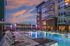 Luxurious apartment complex featuring a stunning pool area with evening lighting, surrounded by modern lounge chairs and city skyline views.