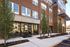 Modern brick apartment complex with large clubhouse entrance, abundant windows, and lush landscaping.