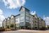 Modern apartment complex with contemporary architecture, featuring large windows and lush landscaping under a bright blue sky.