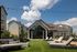 Charming apartment complex with modern outdoor lounge area, cozy seating on lush green lawn, surrounded by elegant architecture under a bright blue sky.