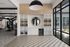 Elegant modern room with large windows, geometric tiles, stylish shelving, and a chic circular mirror, leading into a well-equipped home gym.
