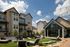Charming modern apartment complex with stylish stone facades and outdoor lounge area under string lights, set against a bright blue sky.