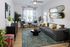 Chic living room with a modern gray sofa, vibrant green and gold pillows, stylish mirrors, and lush indoor plants creating a cozy atmosphere.