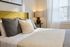 Cozy bedroom with a sunlit window, plush pillows, and an elegant lamp on the side table.