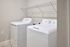 Bright and functional laundry room with modern washing and drying machines, complemented by a practical overhead shelf.