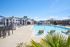 Inviting pool area with comfortable lounge chairs, modern apartments in the background, and bright blue skies.