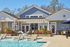 Charming poolside view of a modern clubhouse with cozy hanging chairs and lush landscaping under a clear blue sky.