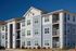 Modern three-story apartment building with blue and white exterior, featuring private balconies and lush landscaping under a clear blue sky.