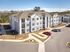 Modern apartment complex with spacious balconies, ample parking, and manicured landscaping under a clear blue sky.
