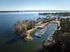 Aerial view of a picturesque marina surrounded by lush trees, with sailboats moored in a calm inlet, offering serene waterfront living.