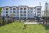 Charming exterior view of modern four-story apartment building with a delightful green space and playful dog, ideal for pet lovers.