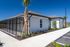 Elegant modern bungalow with fenced patio area, tropical landscaping, and bright exterior under a clear blue sky.