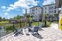 Inviting outdoor patio with Adirondack chairs surrounding a modern fire pit, overlooking tranquil gardens and a pond, set against a backdrop of stylish apartment buildings.