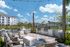Charming outdoor patio featuring stylish seating, modern BBQ grills, and stunning views of a tranquil pond under a bright blue sky.