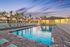 Inviting apartment community pool area at sunset, surrounded by palm trees and modern buildings for a relaxing ambiance.