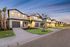 Charming modern townhouses with well-lit facades, framed by palm trees and manicured lawns, creating an inviting neighborhood ambiance at dusk.