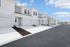 Modern townhouse complex with fresh white facades, a row of garages, and a spacious driveway under a clear blue sky.