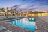 Stunning sunset view over a luxurious swimming pool surrounded by elegant lounge chairs and palm trees, offering a serene resort-like atmosphere.