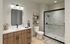 Modern bathroom with sleek wood cabinetry, elegant vanity lights, and a spacious glass shower, complemented by decorative shelving and contemporary tiles.