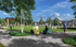 Vibrant communal outdoor space with lush greenery, people enjoying leisure activities, and inviting seating areas under a clear blue sky.