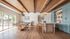 Chic open-concept living area with elegant wooden ceiling, stylish kitchen, and inviting pool table, overlooking lush greenery through expansive glass doors.