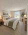 Bright and inviting bedroom featuring a comfortable queen bed with elegant linens, soft lighting, and a large window welcoming natural light.
