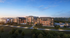 Modern apartment complex at sunset with three distinct buildings labeled Peace, Patience, Kindness, surrounded by lush greenery and a scenic pathway.