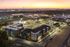 Vibrant aerial view of modern apartment complex with ample parking, set against a stunning sunset backdrop near an airport.