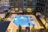 Luxurious apartment complex featuring a sparkling swimming pool surrounded by modern lounge chairs and umbrellas, perfect for relaxation and enjoyment.