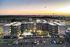Modern apartment complex at sunset with a central courtyard featuring a swimming pool, surrounded by ample parking and lush landscaping, set against a picturesque horizon.