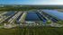 Stunning aerial view of a modern apartment complex with a central lake, sparkling pool, lush green surroundings, and tennis courts for an active lifestyle.