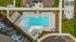 Aerial view of a luxurious apartment complex featuring a stunning outdoor pool area with sun loungers and shaded seating, surrounded by lush green landscaping and modern amenities.