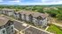 Modern apartment complex with lush landscaping and ample parking, set against a scenic backdrop of rolling hills and green spaces.