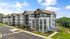 Modern apartment complex with stylish architecture, featuring spacious balconies and ample parking, surrounded by lush greenery under a clear blue sky.