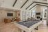 Chic apartment lounge with a stylish pool table, cozy seating area, and fireplace under vaulted beamed ceilings.